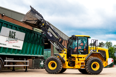 Yellow digger filling a skip.